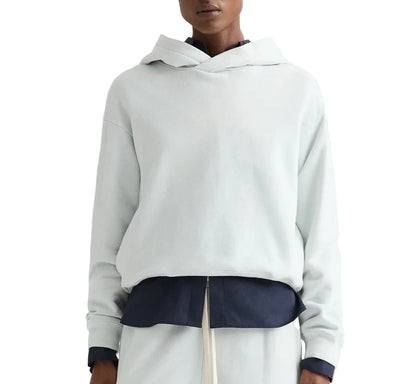 A person wearing a light-colored TWP french terry pullover Hoodie over a dark shirt and light pants, shown from shoulders to waist.