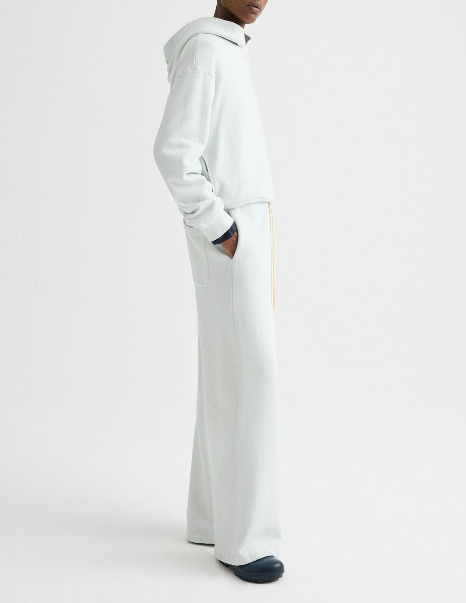A person stands sideways with hands in pockets, wearing a TWP Hoodie and matching wide-leg pants, set against a plain white background.