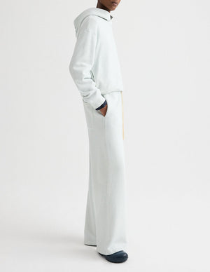 A person stands sideways with hands in pockets, wearing a TWP Hoodie and matching wide-leg pants, set against a plain white background.