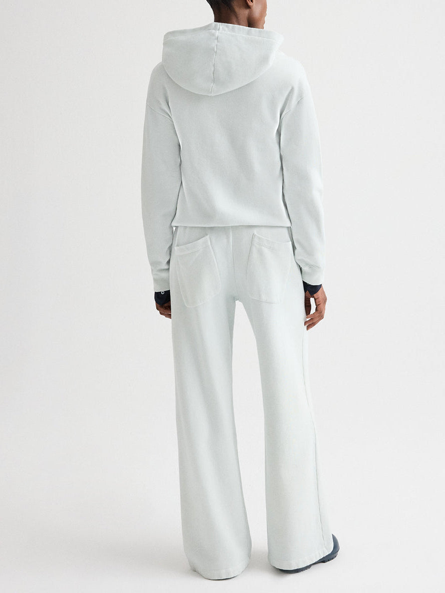 A person stands facing away, wearing TWP's light-colored French terry hooded sweatshirt and matching PJ Pant, set against a plain white background.