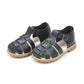 The Boys' Aiden Fisherman Sandal by L'Amour Shoes is a perfect choice for little Aiden's adventures. These black, open-toe sandals feature buckles, brown soles, and are crafted from waxed leather for a stylish yet non-fussy look against a white background.