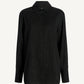 The Mollie Button Down by Kallmeyer is a long-sleeved oversized black shirt featuring a collar and subtle vertical dotted pattern, shown against a plain white background to highlight its relaxed fit.