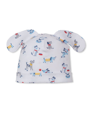 The Kissy Kissy Baby Puppy Patch Novelty Hat is crafted from soft white Pima cotton and features floppy ear details with a playful print of cartoon dogs, food bowls, and bones in blue, gray, red, and yellow for an irresistibly charming look.