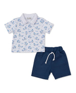 The Boys’ Whale Pods Bermuda Set by Kissy Kissy features a short-sleeve white polo shirt made from soft Pima cotton with a whimsical blue whale print, paired with navy blue drawstring shorts—a charming toddler outfit showcased on a white background.