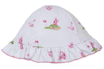The Kissy Kissy Golf Championship Floppy Hat is a white baby sunhat made from soft Pima cotton with a ruffled brim, featuring a whimsical pink and green golf print of carts, clubs, flags, and balls.