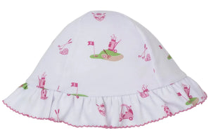The Kissy Kissy Golf Championship Floppy Hat is a white baby sunhat made from soft Pima cotton with a ruffled brim, featuring a whimsical pink and green golf print of carts, clubs, flags, and balls.