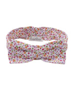 The Kissy Kissy Baby Girls’ Headband is made from soft, stretchy material and features a charming bow with a pink, orange, and green floral pattern on a white background. A small label displays the “Kissy Kissy” brand name.