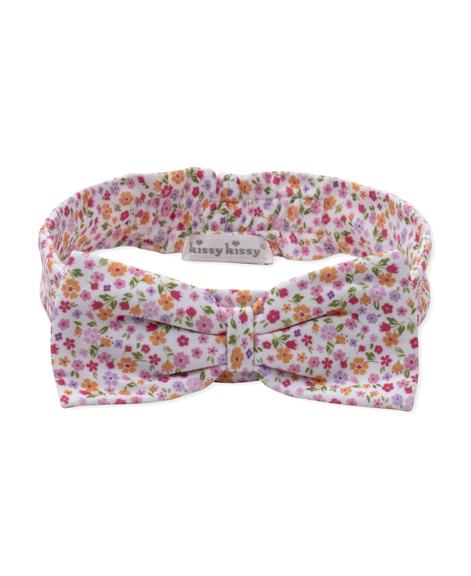 The Kissy Kissy Baby Girls’ Headband is made from soft, stretchy material and features a charming bow with a pink, orange, and green floral pattern on a white background. A small label displays the “Kissy Kissy” brand name.