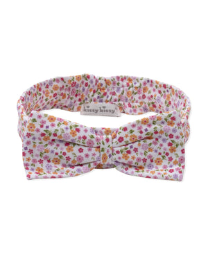 The Kissy Kissy Baby Girls’ Headband is made from soft, stretchy material and features a charming bow with a pink, orange, and green floral pattern on a white background. A small label displays the “Kissy Kissy” brand name.