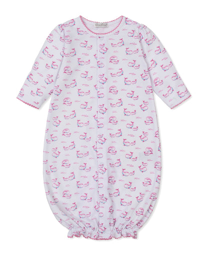 Kissy Kissy Baby Whale Pods Convertible Gown in white Pima cotton, adorned with a delightful pink whale pods print, features long sleeves, pink trim on the cuffs and collar, and an elastic bottom. The sleepwear garment is shown laid flat on a white background.