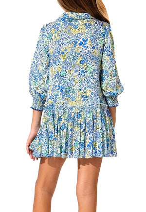 Rear view of a woman wearing a Poupette St Barth Girls' Tesorino Mini Dress with long sleeves and ruffle detailing on the bottom hem, standing against a white background.