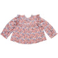 The Pink Chicken Girls' Kalani Top is a long-sleeve blouse featuring the charming Pink Blossom Block Print with pink and red floral patterns on a white background, complete with ruffled shoulders and a round neckline.