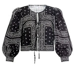 The Katie Top by Hunter Bell NYC is a black bandana-style top with white paisley and geometric prints, balloon sleeves, a round neckline, and a stylish tie-front closure.