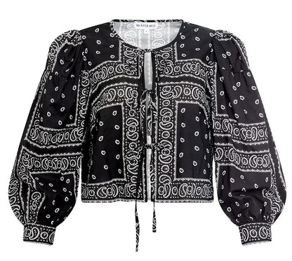 The Katie Top by Hunter Bell NYC is a black bandana-style top with white paisley and geometric prints, balloon sleeves, a round neckline, and a stylish tie-front closure.