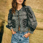 Woman in front of stacked hay bales wears the Hunter Bell NYC "Katie Top," a black bandana-style blouse with balloon sleeves, paired with light blue high-waisted jeans, hands in pockets.