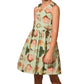 A young girl wears the Girls' June Dress by Hunter Bell NYC, featuring a sleeveless design with a seashell print on a light green background, standing against a white backdrop.