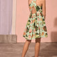 A young girl stands indoors, facing away, wearing the Girls' June Dress by Hunter Bell NYC in the delightful Somers Shell Mint print with crisscross straps, paired with light sandals—a perfect mommy and me summer style.