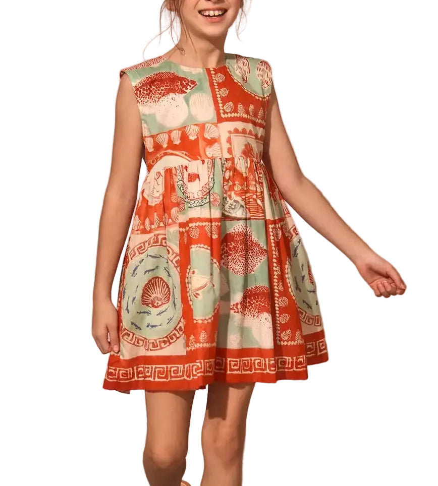 A girl wearing the Hunter Bell NYC Girls' Piper Dress, a sleeveless, knee-length fit and flare dress with an orange, cream, and green pattern featuring geometric and nature-inspired designs.