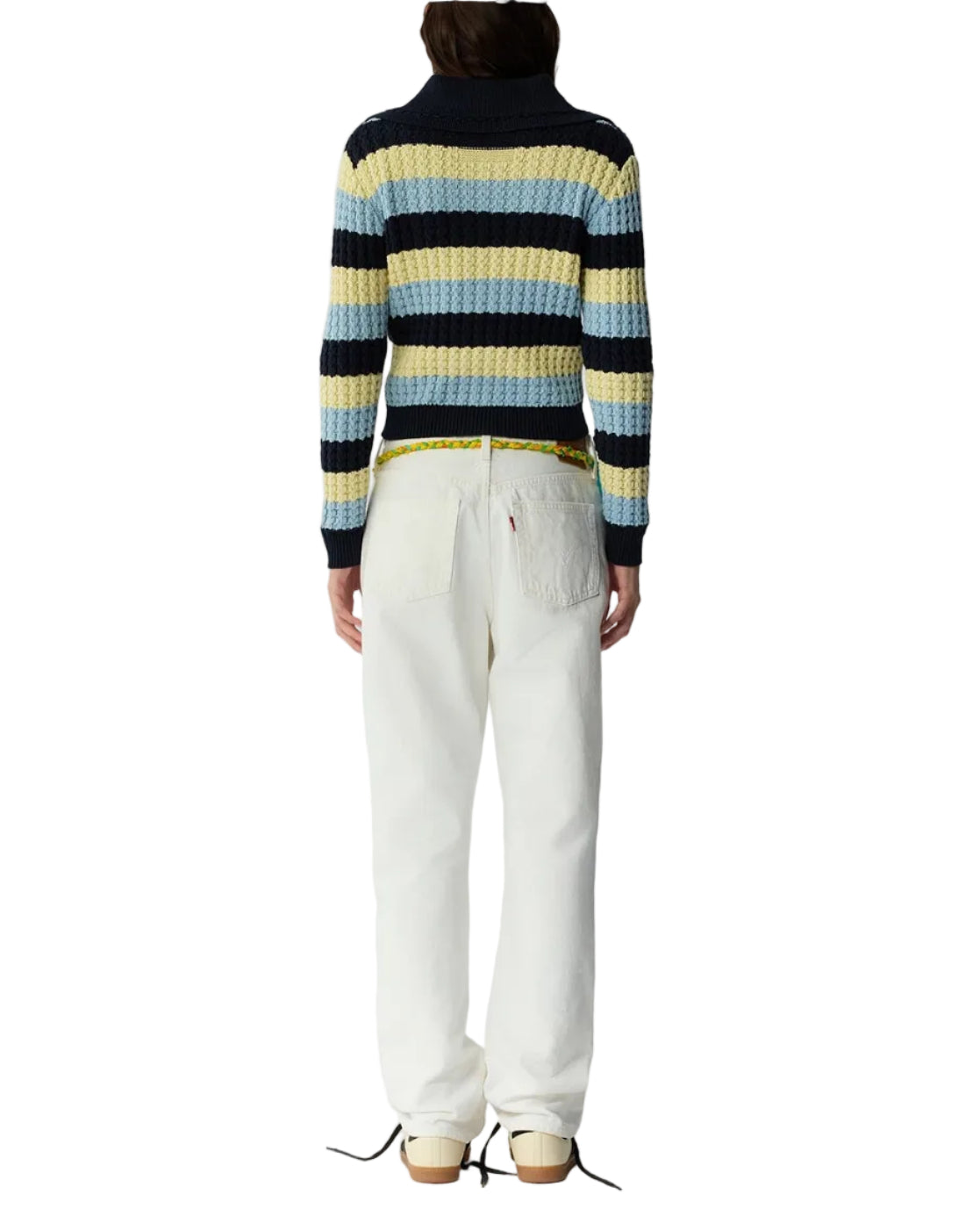 A person stands facing away, wearing the Kirby Jacket by Guest in Residence, paired with white pants, a yellow belt, and beige shoes against a plain white background.