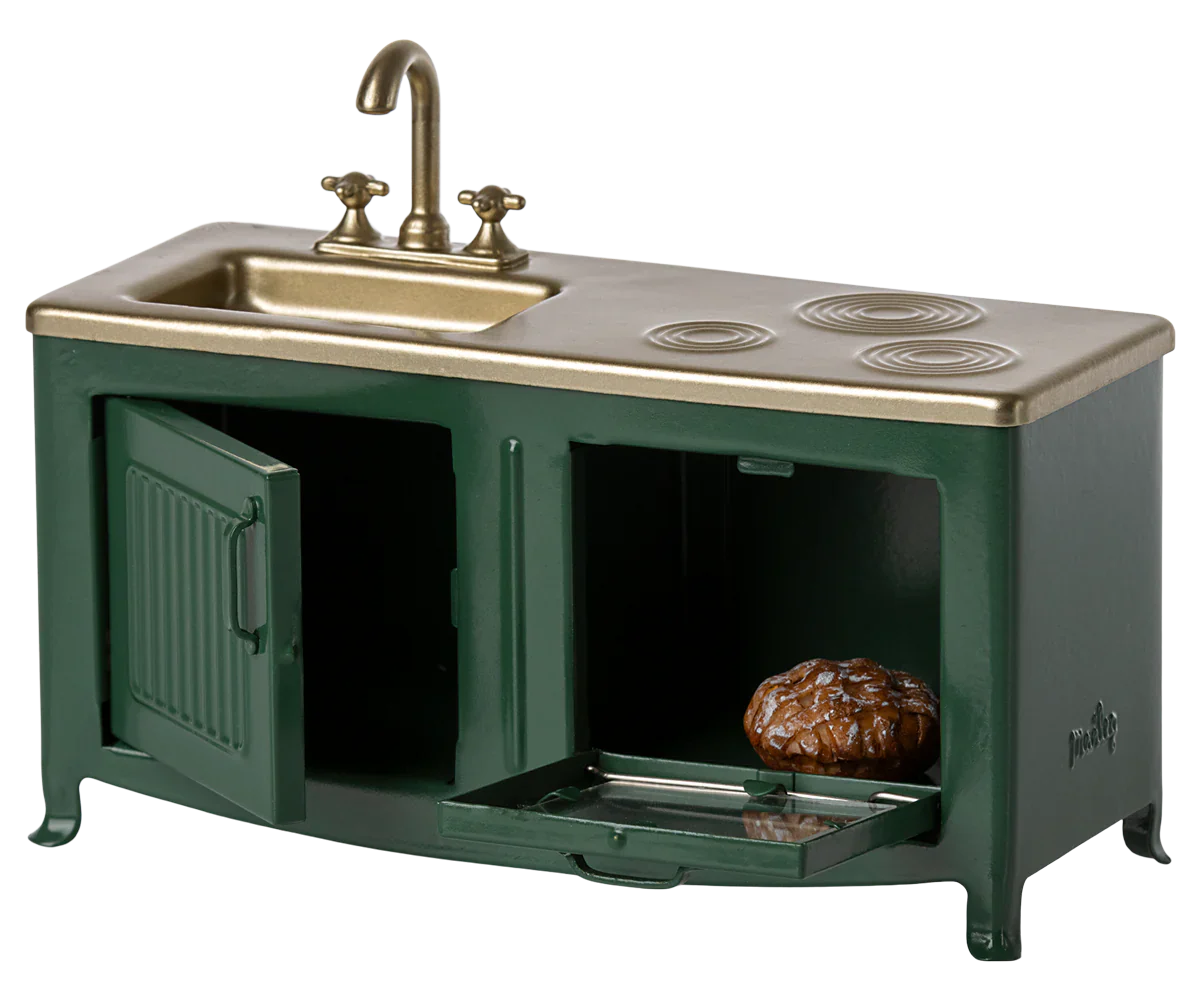 A mini toy kitchen by Maileg, the Maileg Kitchen, Mouse - Dark Green, featuring a green and gold sink, stove, and oven with an open oven door revealing a bun. Perfect for the Mouse family kitchen.