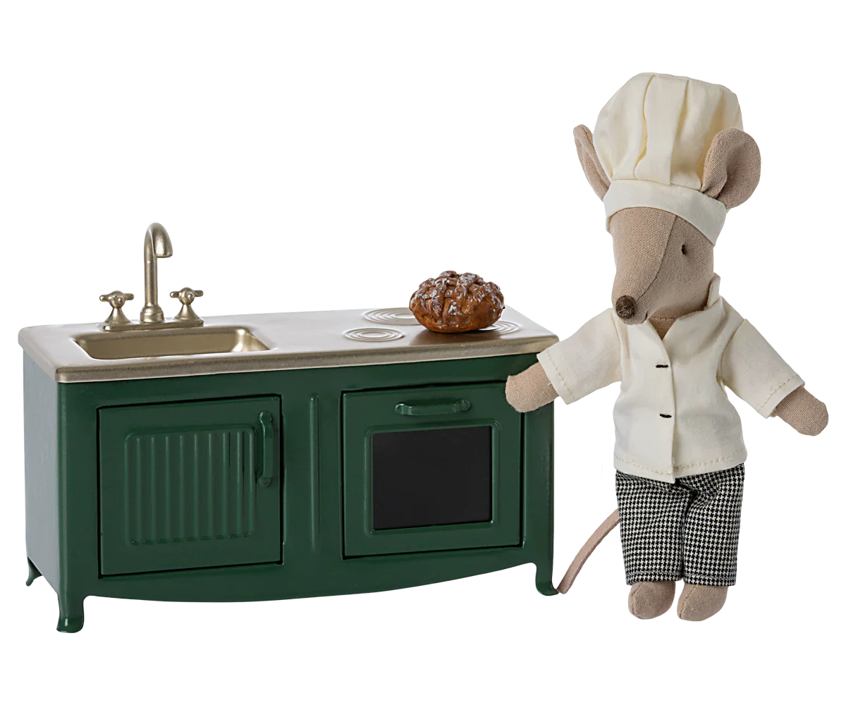 A Maileg stuffed mouse dressed as a chef stands proudly in the Mouse family kitchen beside the Maileg Kitchen for Mice in dark green, complete with a sink, stovetop, and a freshly baked pie.