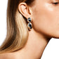 Close-up of a person with long, straight blonde hair wearing shiny, oval-shaped LIÉ STUDIO Klara Earrings made from 925 sterling silver. The background is plain white.