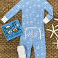 A Baby Boys' Knox's Night Night sleeper by The Beaufort Bonnet Company, paired with white cuffs, white socks, a starfish, and "Boat Book" by Gail Gibbons, is arranged on a woven mat.