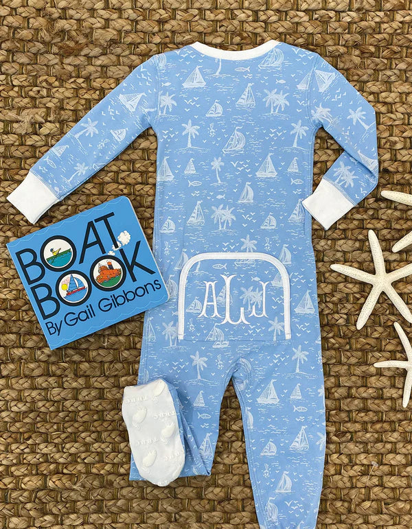 A Baby Boys' Knox's Night Night sleeper by The Beaufort Bonnet Company, paired with white cuffs, white socks, a starfish, and "Boat Book" by Gail Gibbons, is arranged on a woven mat.