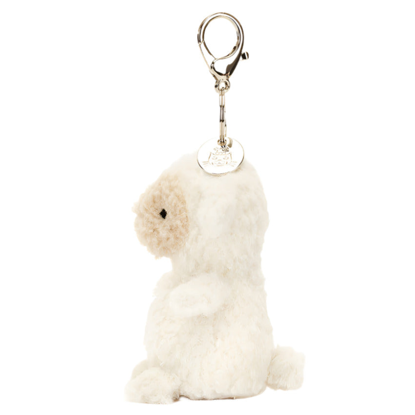 Side view of the Jellycat Little Lamb Bag Charm, showcasing its cream fur and silver clasp. This petite, fluffy keychain by Jellycat adds a charming touch to your accessories.