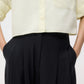 Someone wearing TWP's Carries Trouser paired with a light yellow button-up shirt, hands in their pockets.