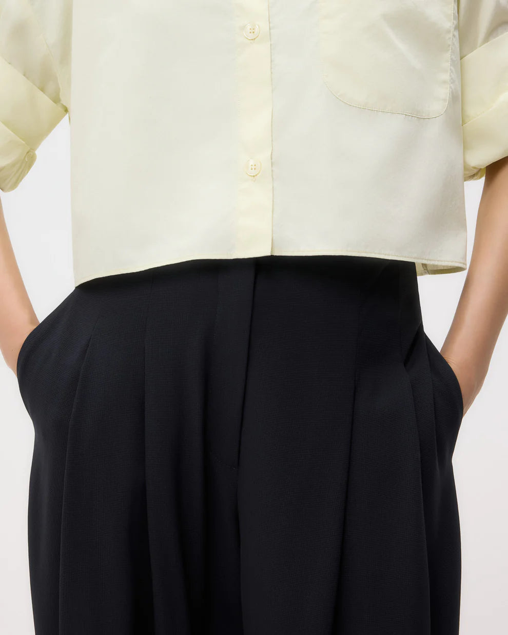 Someone wearing TWP's Carries Trouser paired with a light yellow button-up shirt, hands in their pockets.