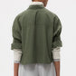 A person is seen from behind wearing the TWP Next Ex Shirt—a vintage-washed green cropped button-down—layered over a light long-sleeve shirt, set against a plain background.
