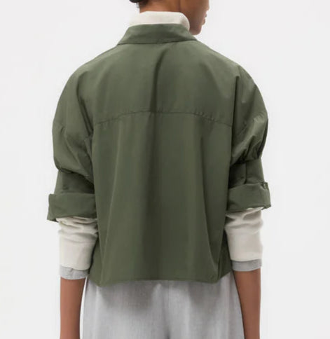A person is seen from behind wearing the TWP Next Ex Shirt—a vintage-washed green cropped button-down—layered over a light long-sleeve shirt, set against a plain background.
