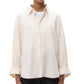 A person wearing the TWP Next Morning Shirt, a relaxed cream-colored oversized button-down over a white top, paired with black pants.