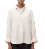 A person wearing the TWP Next Morning Shirt, a relaxed cream-colored oversized button-down over a white top, paired with black pants.