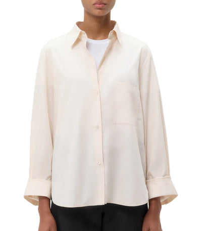 A person wearing the TWP Next Morning Shirt, a relaxed cream-colored oversized button-down over a white top, paired with black pants.
