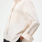 A person wears the TWP Next Morning Shirt—an oversized button-down with a relaxed silhouette, front pocket, and casually rolled-up sleeves—hands in pockets, against a plain background.