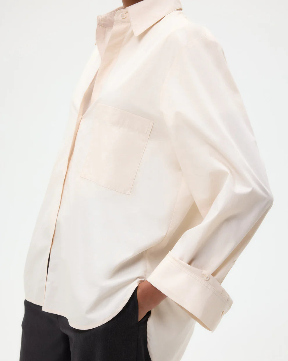 A person wears the TWP Next Morning Shirt—an oversized button-down with a relaxed silhouette, front pocket, and casually rolled-up sleeves—hands in pockets, against a plain background.