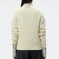 A person is seen from behind wearing the TWP New Jill Crewneck Sweater in cream, styled with a striped shirt and black pants against a plain background.