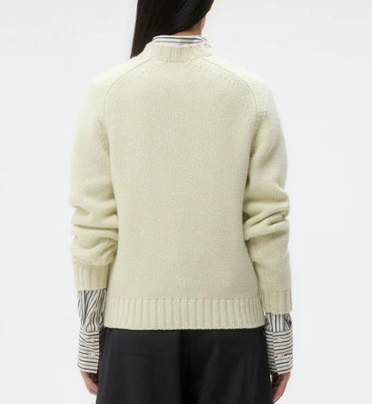 A person is seen from behind wearing the TWP New Jill Crewneck Sweater in cream, styled with a striped shirt and black pants against a plain background.