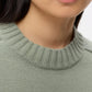 Close-up of a person wearing the TWP New Jill Crewneck Sweater in light green with a boxy fit and ribbed neckline; only their lower face and neck are shown.