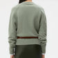 A person with long dark hair is shown from the back, wearing TWP's New Jill Crewneck Sweater in light green and a dark green skirt against a plain background.