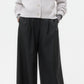 A person wearing the TWP Cropped Cashmere Cardi in gray, styled with wide-leg black trousers and brown shoes, stands against a plain white background.
