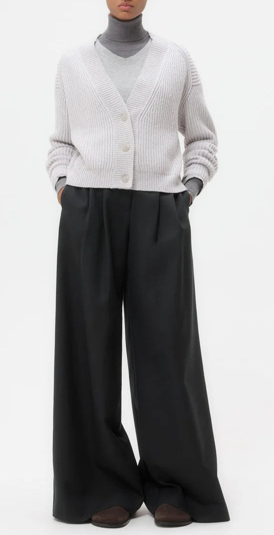 A person wearing the TWP Cropped Cashmere Cardi in gray, styled with wide-leg black trousers and brown shoes, stands against a plain white background.