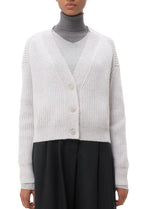 A person wears the TWP Cropped Cashmere Cardi, a light gray ribbed button-up cardigan, over a gray turtleneck and top with dark pants.