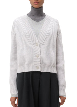 A person wears the TWP Cropped Cashmere Cardi, a light gray ribbed button-up cardigan, over a gray turtleneck and top with dark pants.