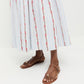 A person wearing stylish timber brown Lara Sandals by Loeffler Randall and a white and light blue striped skirt with red floral patterns stands on a white background.