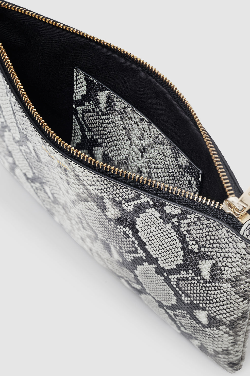 A close-up of the Elly Large Pouch by Anine Bing shows a black and grey snakeskin print with an open view revealing its inner pocket.