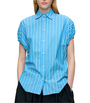 A woman wears the Callas Milano Lecce Stripe Top, a relaxed fit blue and white striped short-sleeve button-up shirt, paired with black pants.