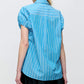 A person is seen from the back wearing the Lecce Stripe Top by Callas Milano, a relaxed-fit blue and white striped short-sleeved shirt, styled with a black skirt against a light background.